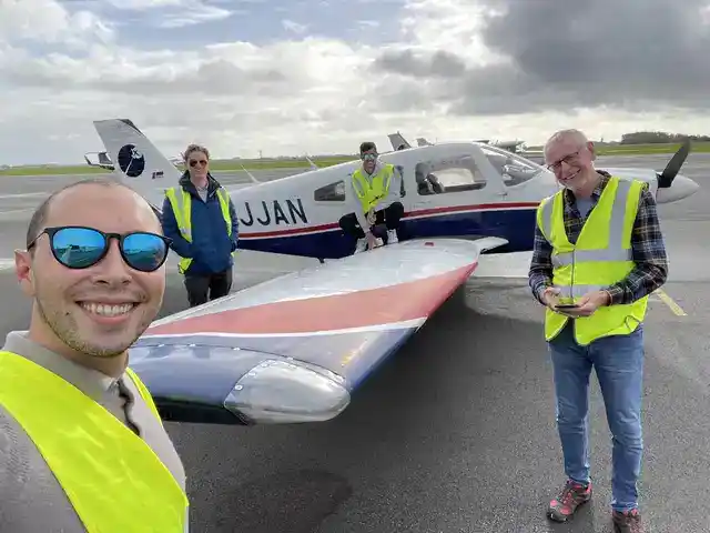 Four people in high-visibility vests beside a light aircraft at an airfield.