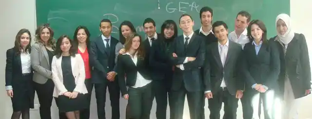 A group dressed in suits standing in a classroom in front of a board marked GEA.