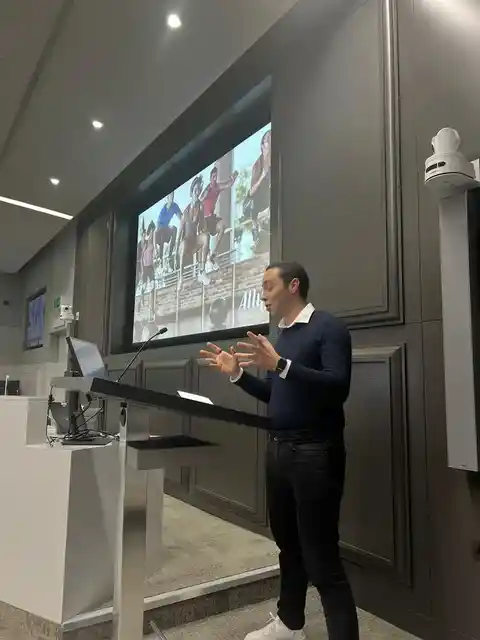 A speaker presenting from a lectern beside a projected slide.
