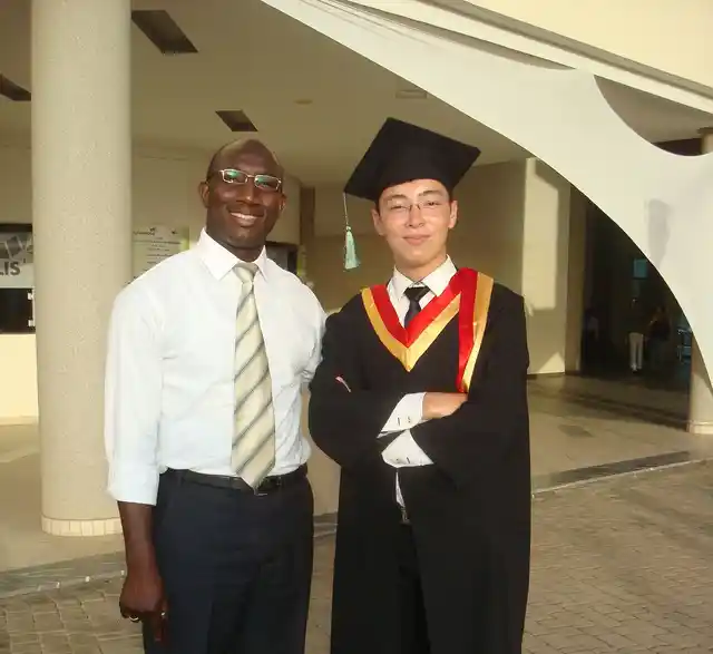 A graduate in a cap and gown standing beside another person.