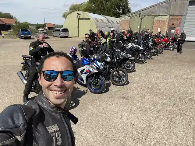 A group of motorcyclists gathered with their bikes outside a workshop.