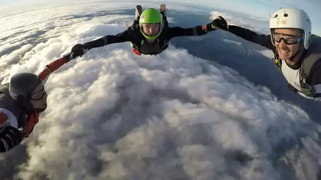 Three skydivers holding hands in freefall above a layer of clouds.