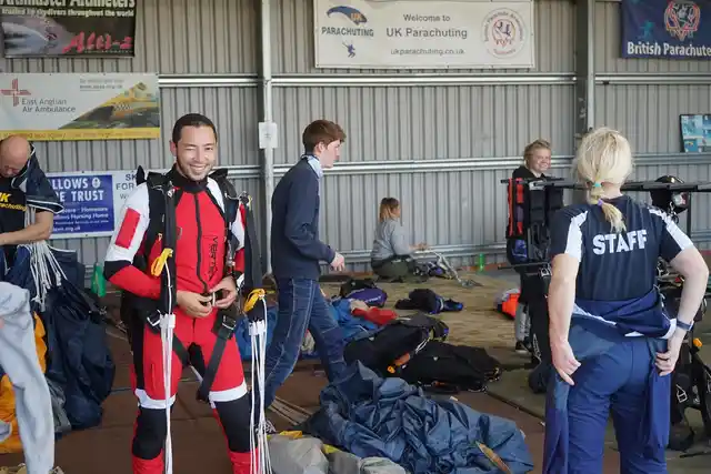 A skydiver in a red jumpsuit and parachute harness getting ready inside the hangar.