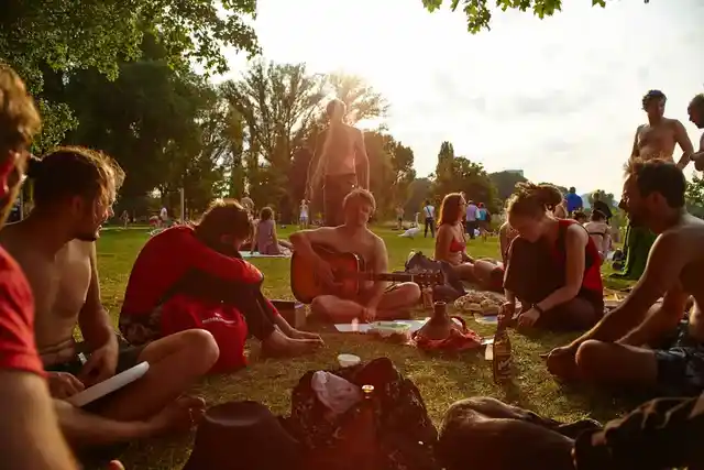 A group relaxing on grass in a sunny park, with one person playing a guitar.
