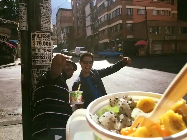 Two friends smiling beside a city street, with a cup of fresh fruit in the foreground.